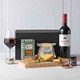 Gourmet Wine & Cheese Gift Box. A wooden serving board displays an assortment of gourmet snacks, including crackers, grapes, and two types of cheese. Beside it, a bottle of red wine is positioned with a serving glass filled with the wine. The items are presented against a neutral background, adding elegance to the arrangement. A black box is visible in the background. Gourmet Wine & Cheese Gift Box. A wooden serving board displays an assortment of gourmet snacks, including crackers, grapes, and two types of cheese. Beside it, a bottle of red wine is positioned with a serving glass filled with the wine. The items are presented against a neutral background, adding elegance to the arrangement. A black box is visible in the background.
